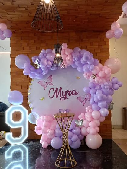 A beautiful butterfly-themed party for a 9th birthday. This setup features a circular backdrop with a pink and purple balloon arch and a large light-up number '9'.