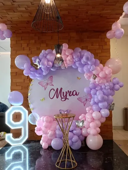 A beautiful butterfly-themed party for a 9th birthday. This setup features a circular backdrop with a pink and purple balloon arch and a large light-up number '9'.