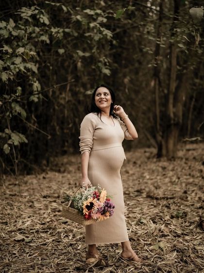A joyful portrait of the mom-to-be in a sun-dappled forest, looking up with a happy expression while holding a colorful bouquet.