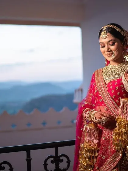 A stunning portrait of my bride Kashish against the backdrop of the Udaipur mountains. Her traditional pink and red lehenga is paired with a classic bridal makeup look, featuring a defined eye, a small bindi, and a warm glow.