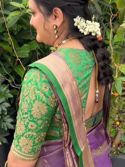 A client wearing a vibrant green blouse with heavy gold floral embroidery, paired with a purple Kanchivaram saree.