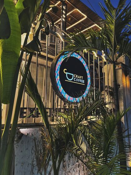 The neon sign of 'Craft Coffee' at night, surrounded by palm trees, creating a cool, tropical vibe.
