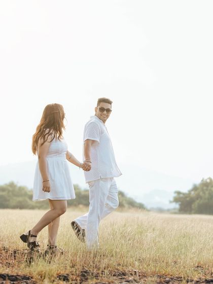 A candid shot of the couple walking hand-in-hand through a field, capturing a natural and unposed moment of connection.