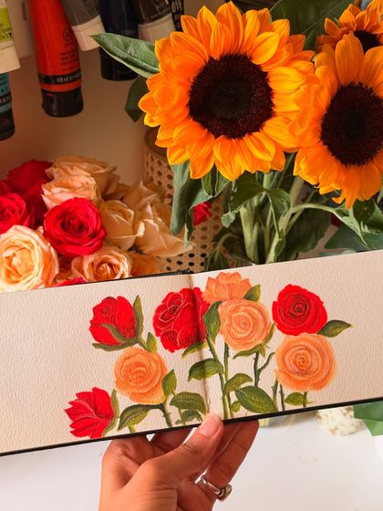 Holding the finished sketchbook painting next to the real sunflowers and roses that inspired it. You can see how I translated the colors and forms of the fresh flowers directly onto the page using gouache.