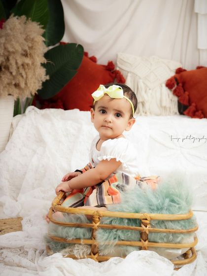 A close-up portrait of a baby girl in a basket, showing off her cute outfit and curious expression.
