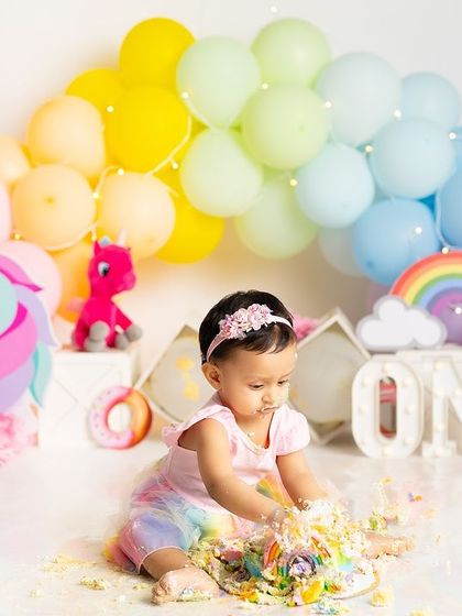 The cake smash is underway! This little one is fully enjoying her rainbow-themed first birthday, with cake and frosting creating a wonderfully messy and happy scene.