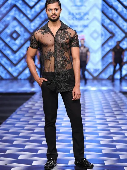 A full-length shot on the runway for Ramesh Dembla, wearing a sheer lace shirt that blends sensuality with high fashion.