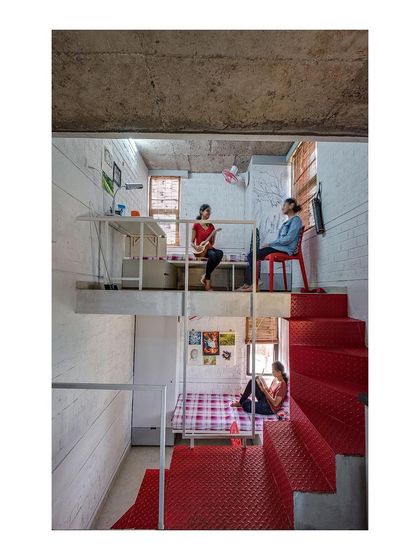 The interior of a unit in the "Stacked Student Housing" project reveals a split-level layout that maximizes space. A simple palette of whitewashed brick, bare concrete, and a red steel staircase is both frugal and expressive.