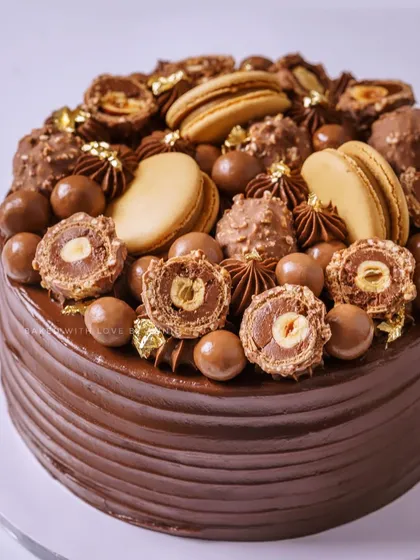 A closer look at my Hazelnut Praline Feuilletine cake, topped with sliced Ferreros, macarons, Maltesers, and a touch of 24k edible gold leaf for extra opulence.
