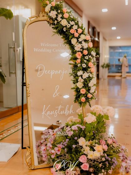A personalized welcome sign on a gold-framed mirror, adorned with a beautiful arch of pastel flowers. This elegant detail sets a sophisticated tone for the wedding ceremony.