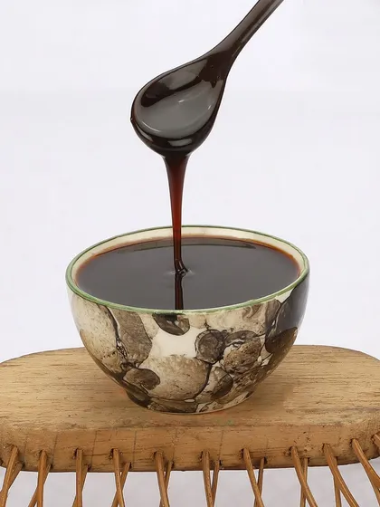 This action shot captures the thick, viscous texture of a food syrup as it's poured from a spoon into a bowl, ideal for highlighting product quality.