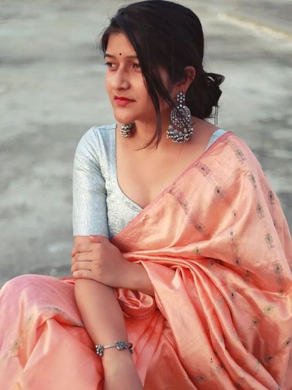 A quiet, contemplative portrait of a woman in a peach saree, seated outdoors. Her gaze is directed away from the camera, suggesting she is lost in thought, embodying the feeling of finding fullness after moments of emptiness.