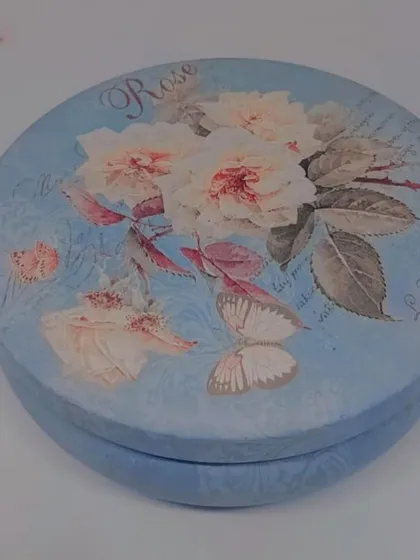 The lid of a vintage-style floral tin candle. The beautiful design means the container can be reused long after the candle is gone.