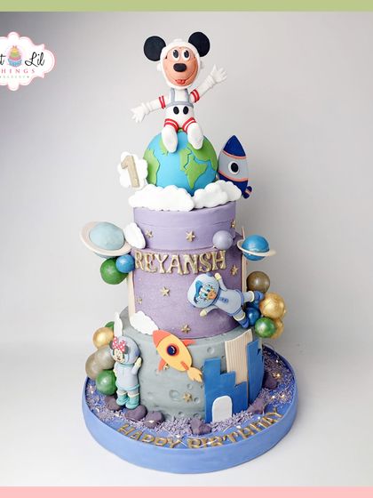 An out-of-this-world space adventure cake for a first birthday. This three-tiered masterpiece features Mickey Mouse as an astronaut, planets, rockets, and other cosmic details.