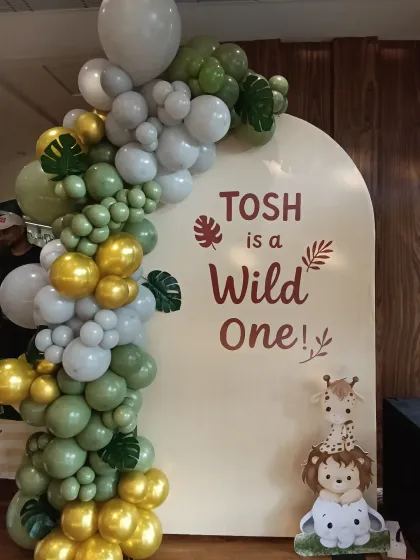 The 'Wild One' jungle theme is a huge hit for first birthdays. Here, I used an organic balloon arch in sage green, white, and gold around a custom arched panel, complete with cute jungle animal cutouts.