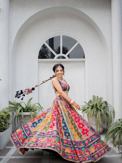 The bride twirls in her vibrant, multi-colored Mehendi lehenga, her long braided hair adding to the playful movement.