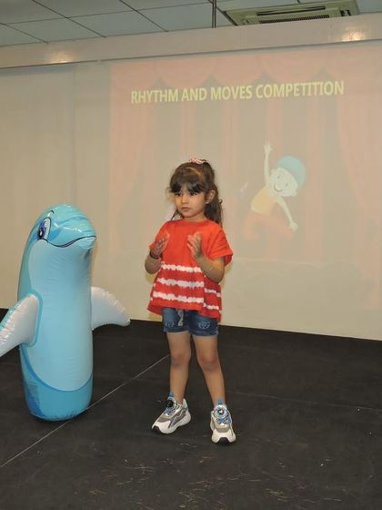 A student shares the stage with an inflatable dolphin prop, adding a playful element to her dance performance.