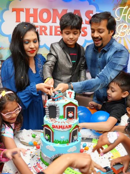 The whole family helps Damian cut his rotating Thomas & Friends cake, surrounded by excited friends.