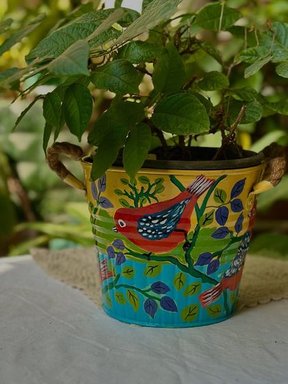 One of a new set of metal planters painted by my mom. This one features a bright red bird against a sunny yellow background, with rustic rope handles.