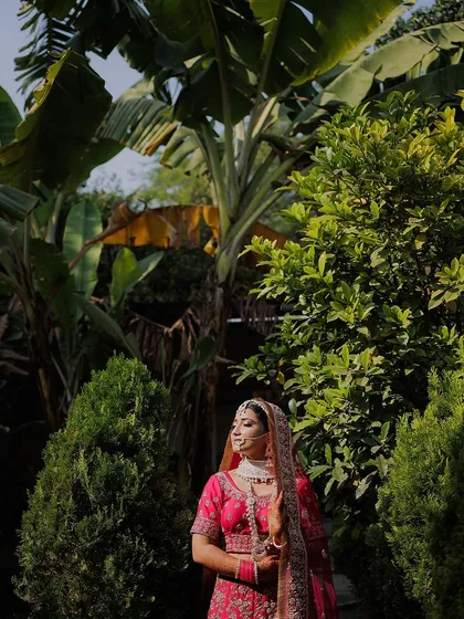 A bride stands amidst lush greenery, the natural light highlighting her vibrant pink lehenga. This portrait showcases our ability to use natural environments to create stunning bridal shots.