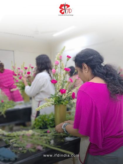 A student carefully adds pink carnations to her vertical arrangement. This photo captures the concentration and hands-on nature of our classes, where you learn by doing.