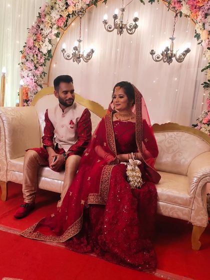 The couple seated on the stage, looking perfect for their reception. The bride's makeup is designed to be seen beautifully from a distance.