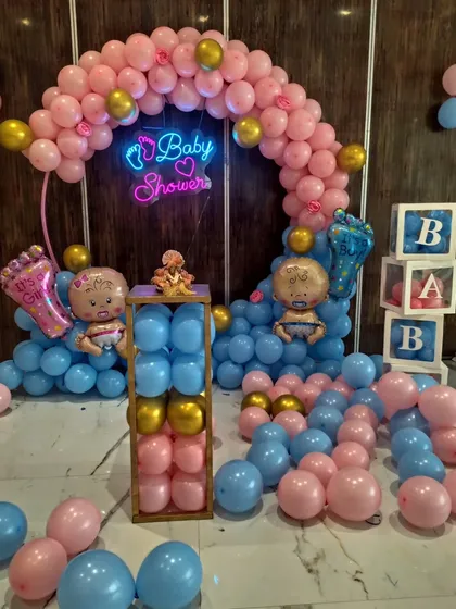 A pink and blue baby shower setup with a neon sign, balloon columns, and "BABY" blocks.