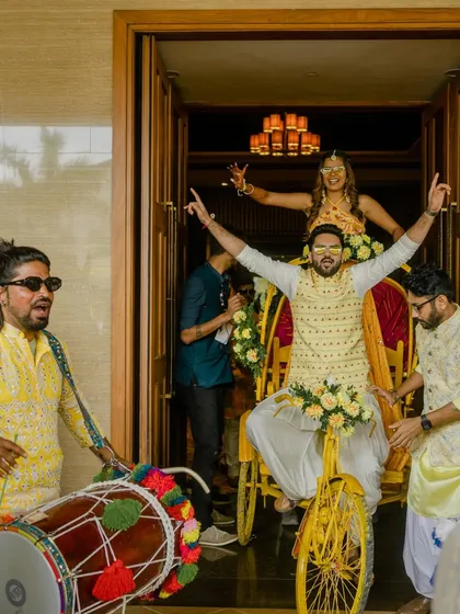 The couple making a grand entry on their decorated rickshaw, with a dhol player adding to the festive atmosphere.
