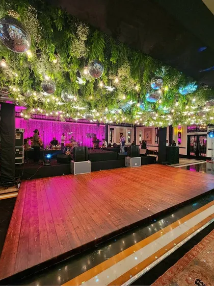 We create the perfect party atmosphere with elements like this expansive wooden dance floor set under a ceiling of hanging greenery and disco balls. The pink and purple lighting sets the mood for a night of dancing.