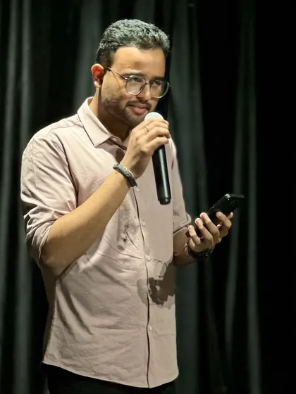 A performer shares his art with the audience, holding a microphone and his phone. This candid shot captures the raw and authentic talent showcased at our community events.