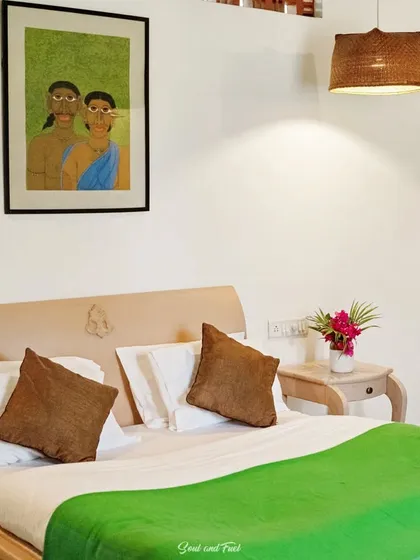 A simple and serene bedroom at Z Farms, with a pop of green on the bed and a beautiful piece of traditional Indian art on the wall. The decor is minimalist yet culturally rich.