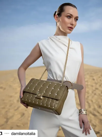 A Spring Summer campaign image for Da Milano, shot in the Jaisalmer dunes. The model is styled in a clean, white jumpsuit, providing a perfect neutral canvas for the olive green studded handbag to stand out.