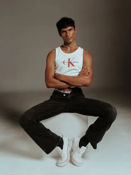 A full-length seated pose that showcases the complete Calvin Klein look, from the tank and jeans to the classic white sneakers. This composition is designed to feel both relaxed and powerful, a key theme in my menswear direction.
