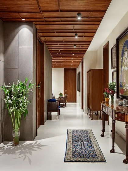 This corridor in the B-10 Residence showcases understated elegance. A sophisticated timber false ceiling conceals services while adding warmth, and the restrained material palette is enriched by the owner's collection of traditional art.