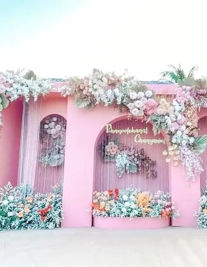 A stunning pink structure for a daytime event, heavily adorned with cascading arrangements of pastel flowers. The arched niches are also filled with floral designs, creating a beautiful and romantic photo wall.