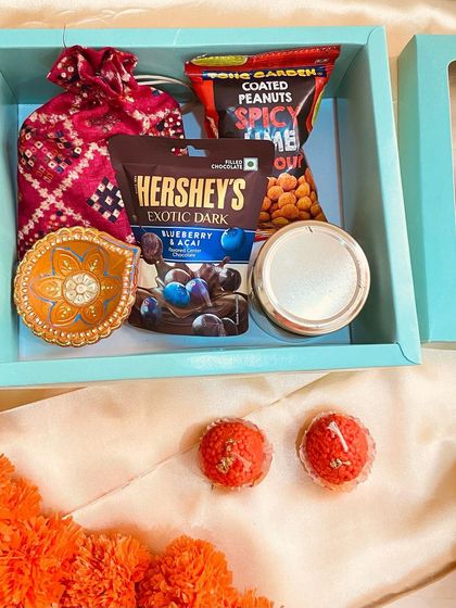 A lovely teal gift box containing a mix of sweet and savory treats like Hershey's exotic dark chocolates and spicy coated peanuts, along with a hand-painted diya.
