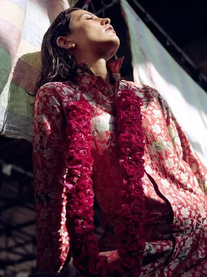 A shot from the 'Phool Mandi' series, where the model is styled in a red floral suit and a fresh rose garland. The play of light and shadow in the market setting adds a raw, atmospheric quality to the image.