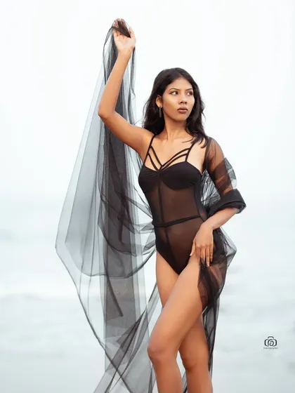 A graceful pose with the model holding a long piece of sheer black fabric that billows in the wind. The overcast sky adds a moody and dramatic feel to this beach portrait.
