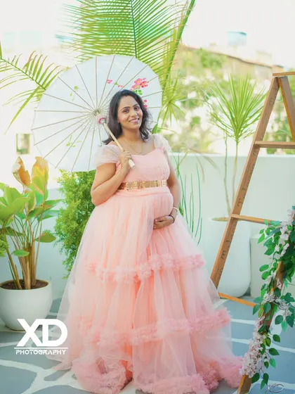 An elegant solo portrait of the mother-to-be in a peach gown, holding a paper umbrella in a bright studio setting.