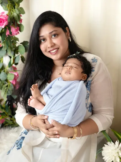 A beautiful family portrait with mom holding her newborn, both looking at the camera. The floral setup adds a soft, dreamy touch to the photo.