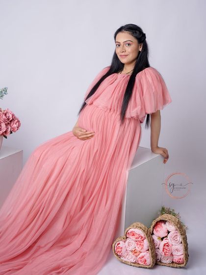 A lovely three-quarter portrait. The mom-to-be's gentle smile and the soft pink gown create a warm and inviting image.