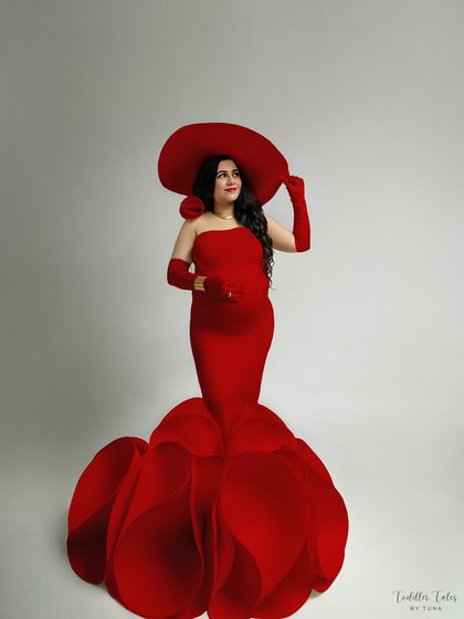 A full-length view of the magnificent red flower gown. The sculptural petals create a stunning silhouette, transforming the mother-to-be into a living bloom. This is a true couture maternity statement piece.