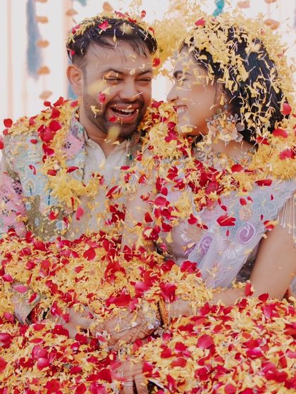 A joyful, candid shot of the couple laughing as they are showered with flower petals during their Haldi.