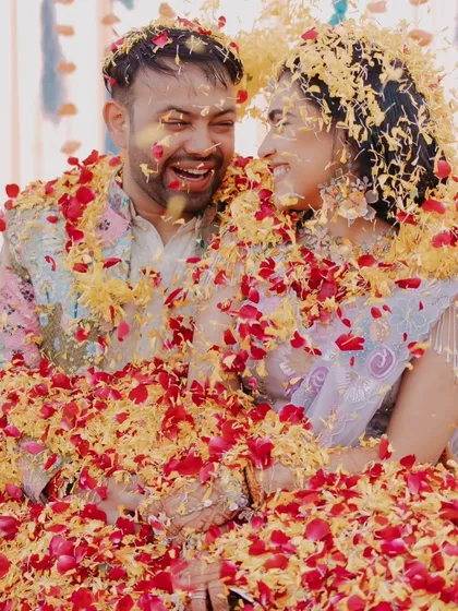 A joyful, candid shot of the couple laughing as they are showered with flower petals during their Haldi.