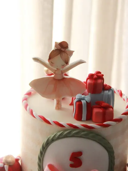 A close-up of the delicate ballerina topper on the Christmas-themed birthday cake.