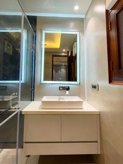 The vanity area in the dark-tiled bathroom. A backlit mirror provides excellent task lighting, while the simple white vanity keeps the focus on the dramatic shower wall.