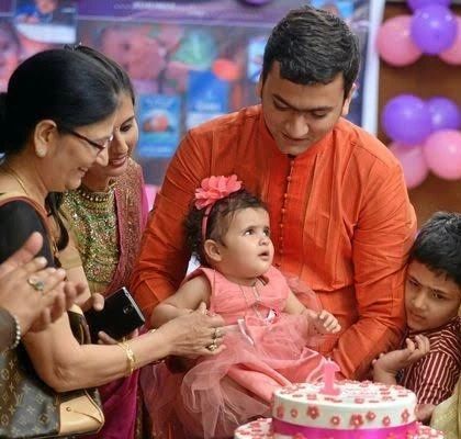A candid, multi-generational photo capturing the family's attention on the birthday girl as she sits by her cake.
