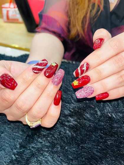 A festive red set with a mix of finishes. This look includes glossy red nails, sparkling pink and red glitter accent nails, and fun details like candy cane stripes and a 3D gold star.