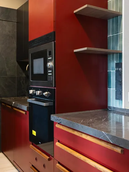 This kitchen makes a bold statement with its Marsala red cabinetry. Paired with dark stone countertops and open wooden shelves, the look is dramatic yet sophisticated, perfect for a client who loves confident design choices.