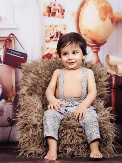 A relaxed toddler poses in a miniature armchair during his vintage-themed session.